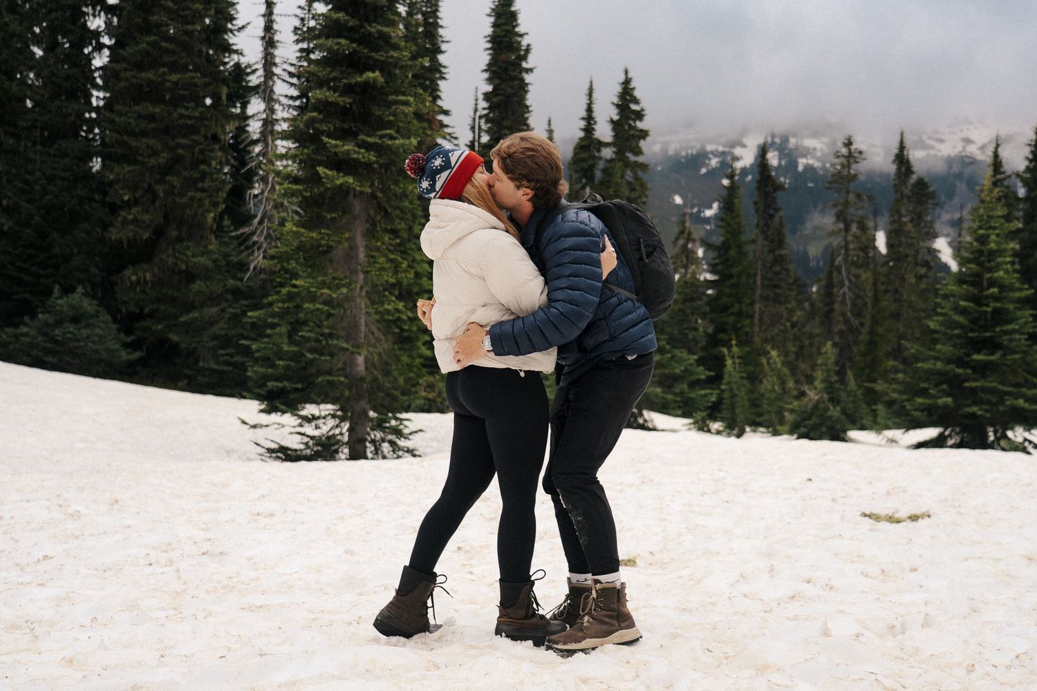 Two people snowshoeing through a snowy forest trail with evergreen trees in the winter landscape.