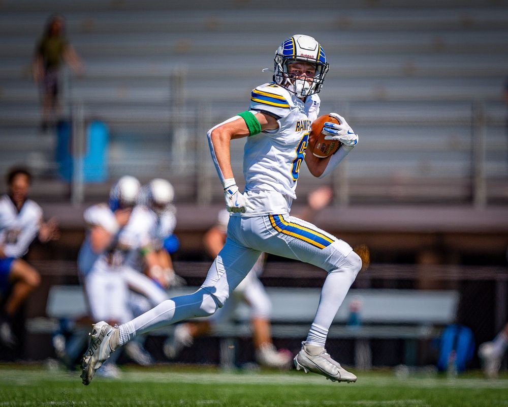 Football player in white uniform and blue helmet runs with ball during competitive game on sunny field.