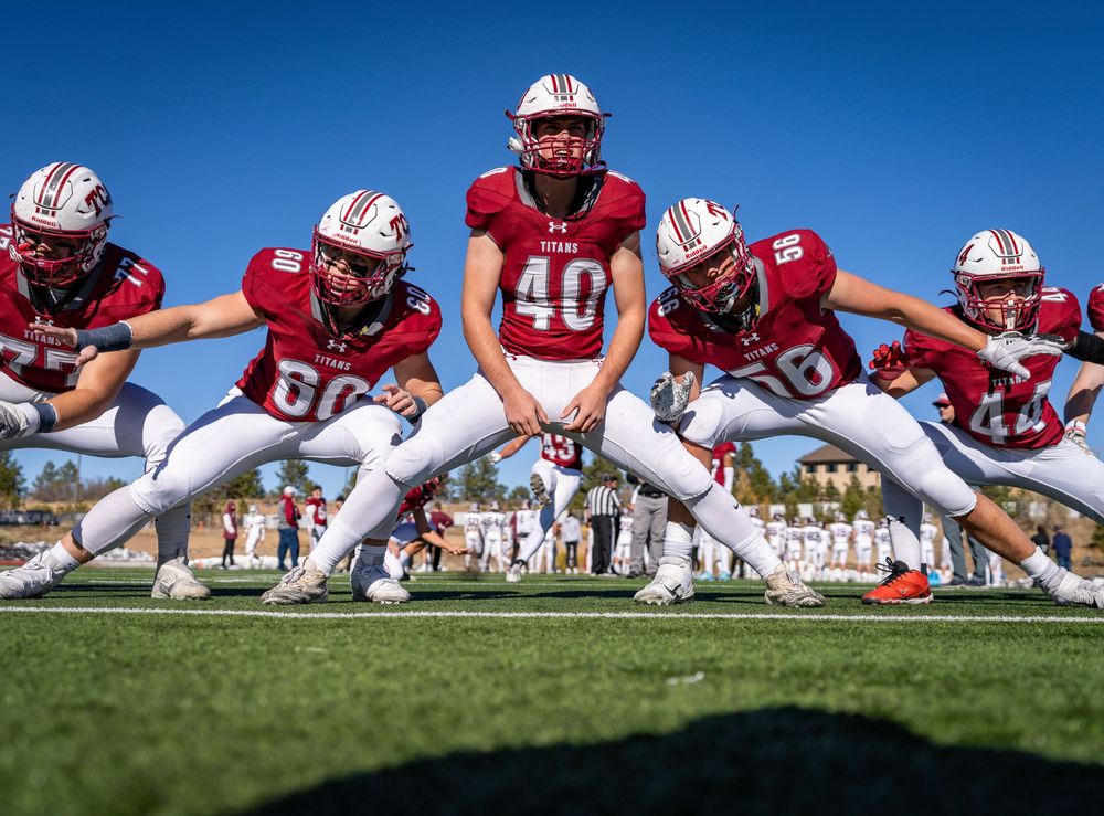 Football players lined up in defensive stance on grass field against bright blue sky background.