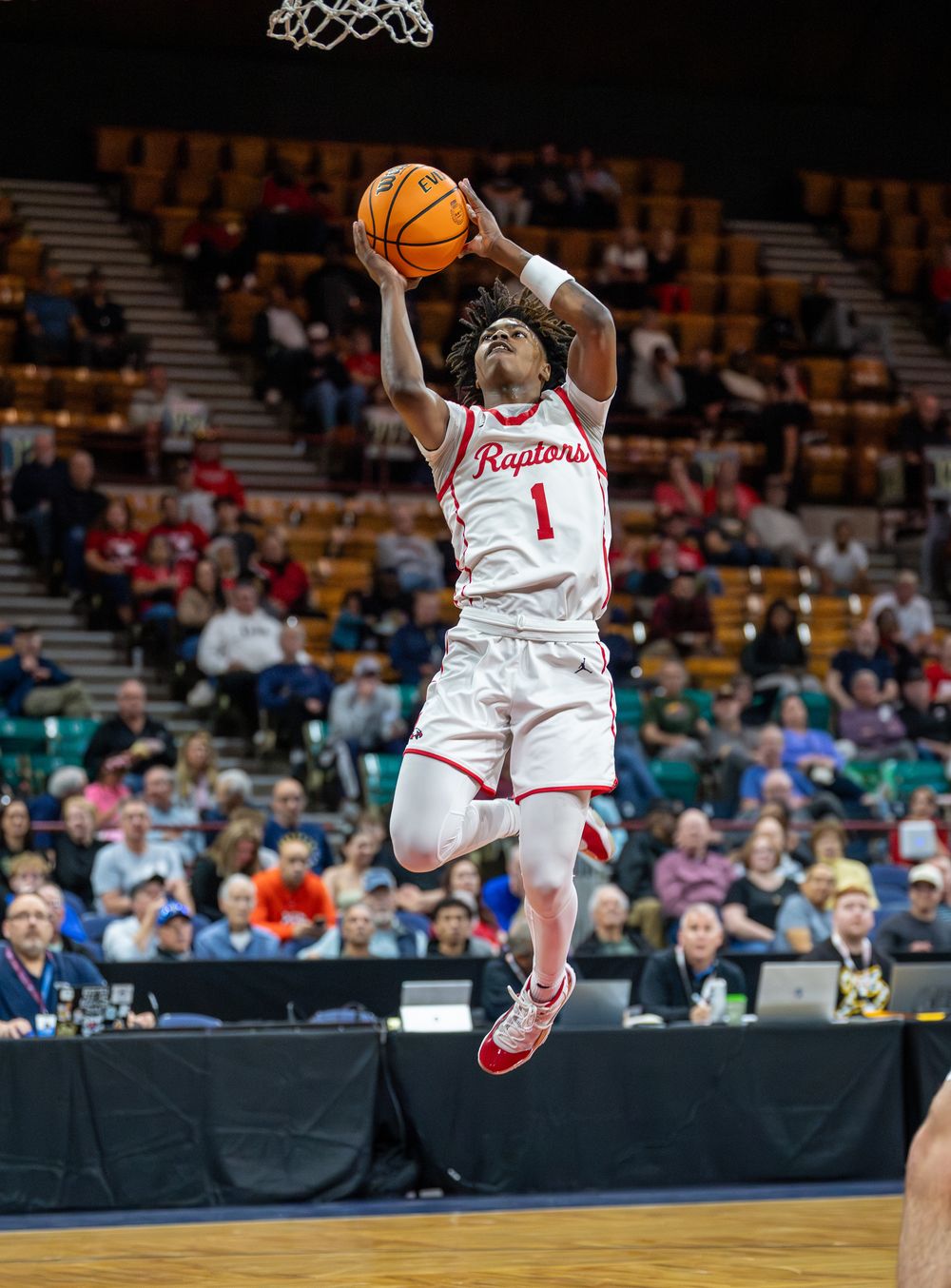Basketball player in white jersey makes a dynamic leaping motion to score during a game.