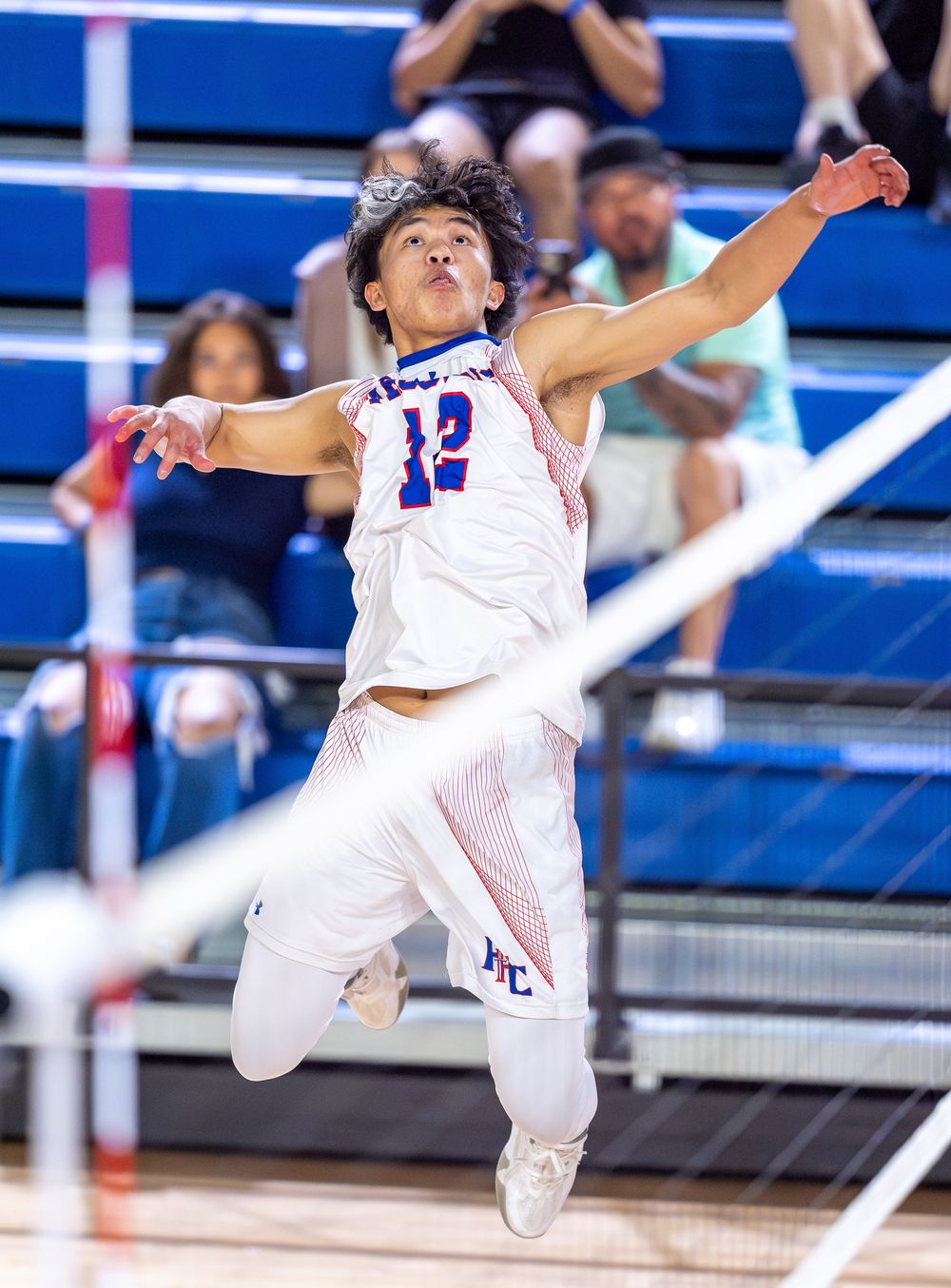Basketball player in white jersey number 12 leaps high to spike volleyball during intense indoor match.