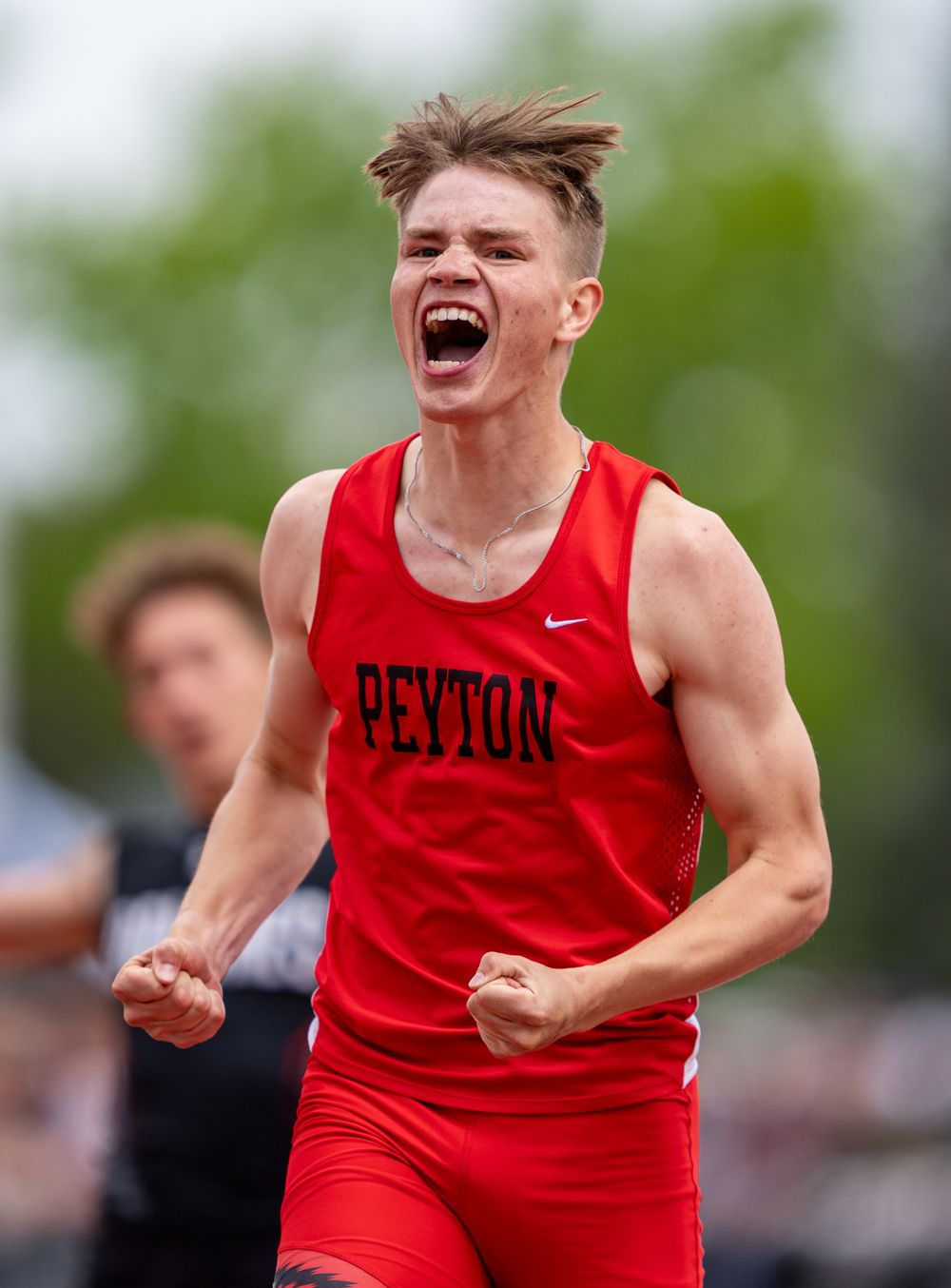 Athletic competitor in red Nike tank top celebrates with intense emotion during outdoor sports event.