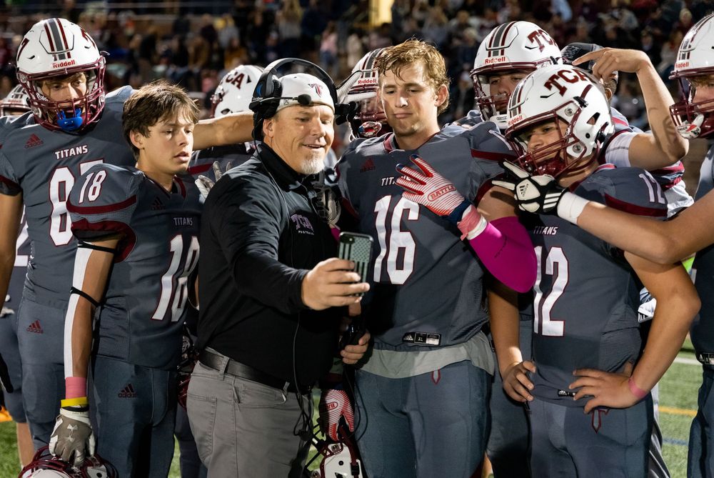 A football team huddles together in their dark uniforms during a game celebration on the field.