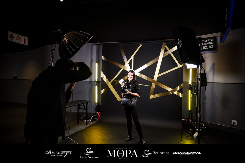 A model poses in a photography studio with geometric light installations and professional lighting equipment in a dark setting.