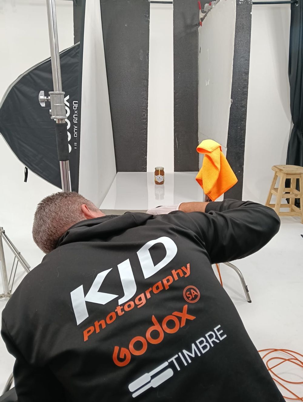 Photographer from KJD Photography, sponsored by Godox, cleaning a product in a professional white photography studio.