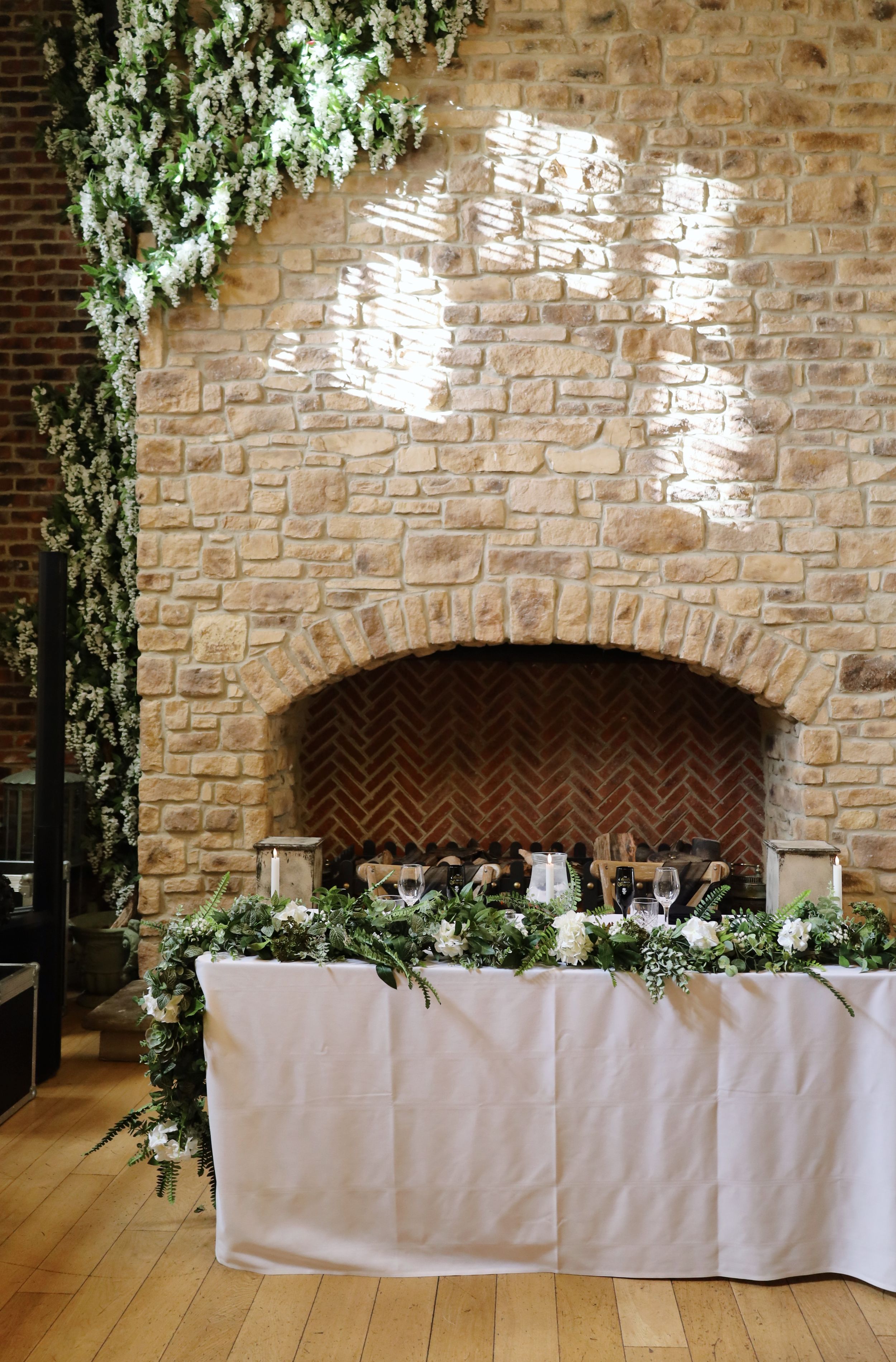 Wedding reception head table setup against stone wall with floral decorations and string lights.