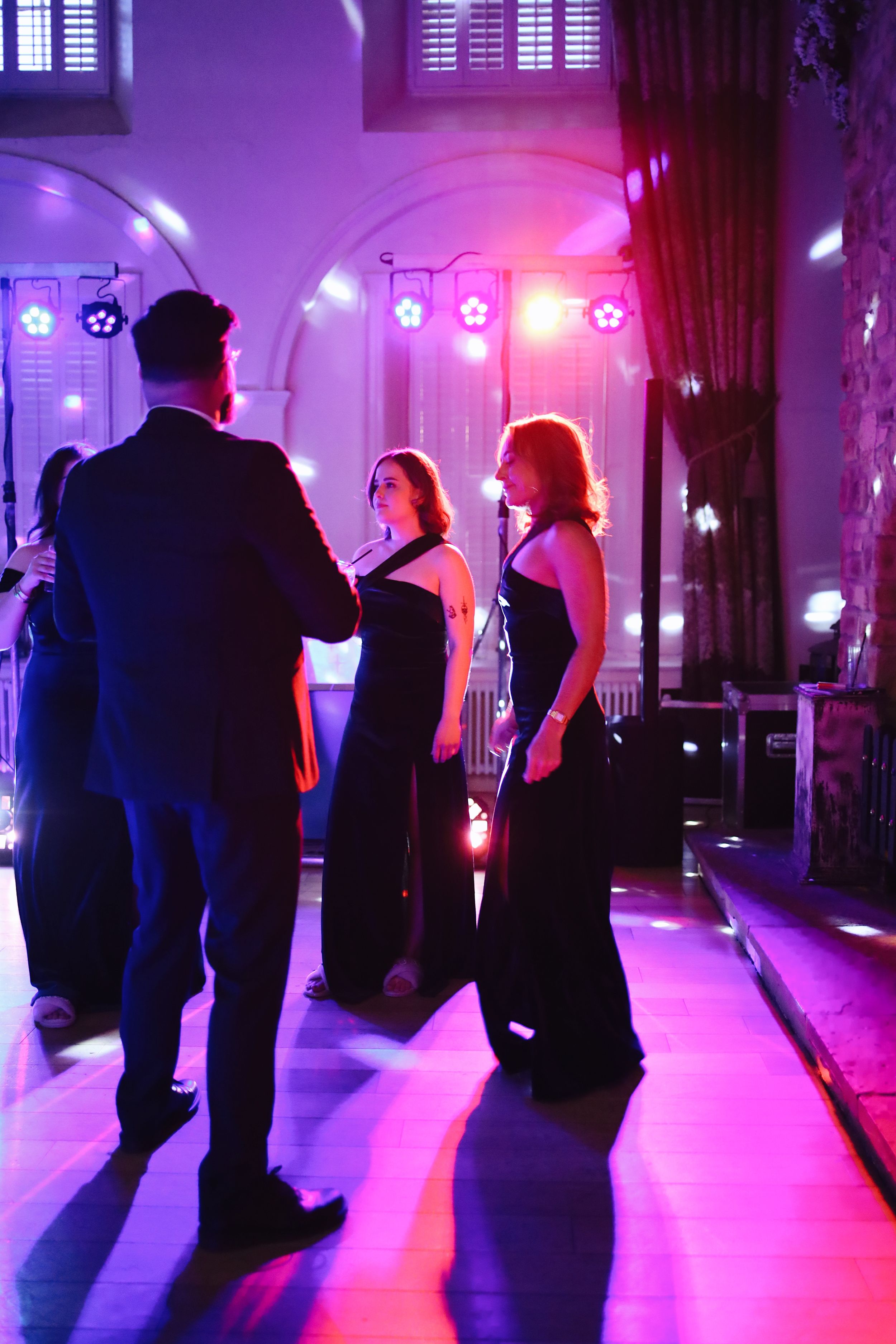 Dance floor scene bathed in purple and pink lighting at evening wedding reception.