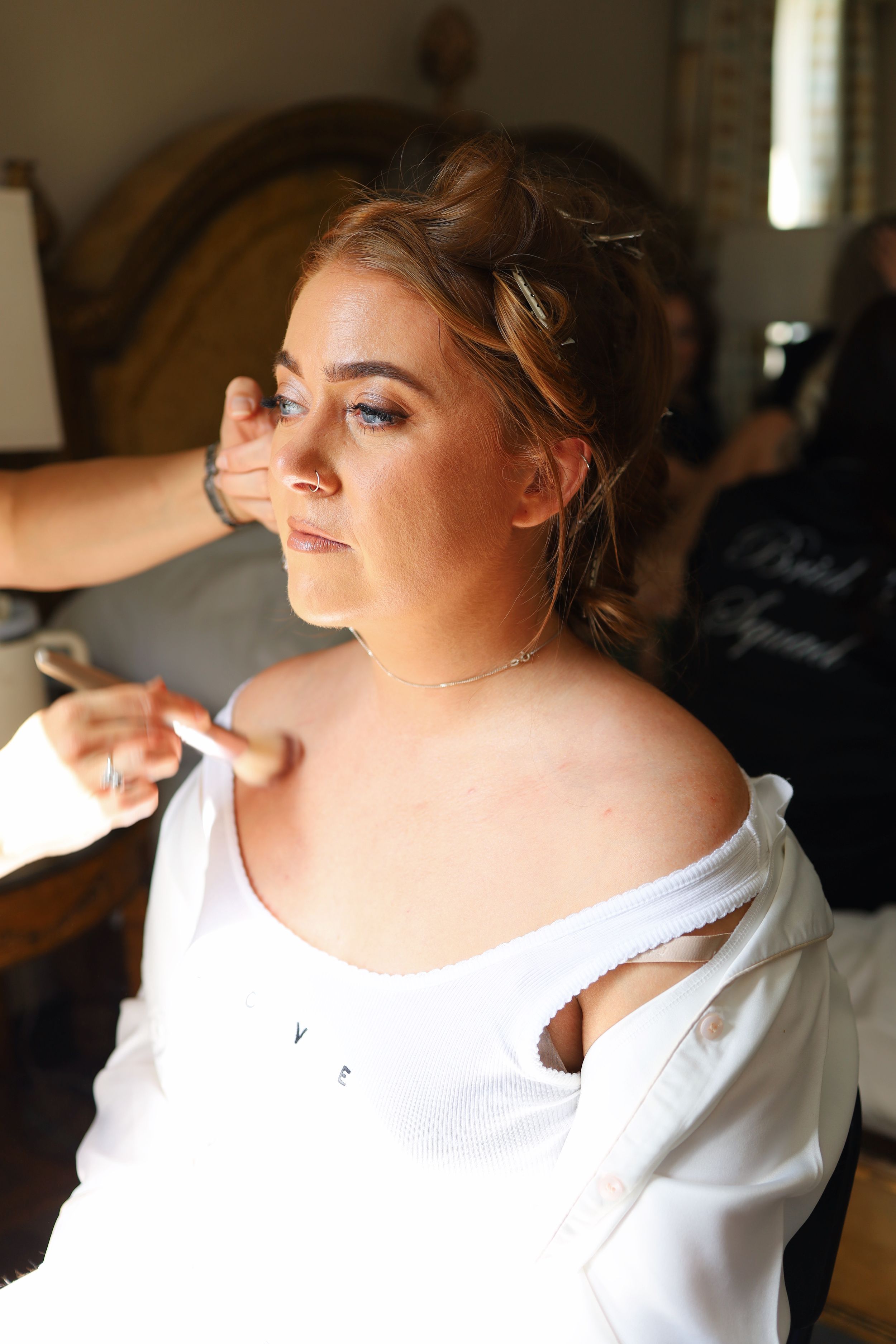 Bride getting ready in a white robe with soft lighting in morning preparation.
