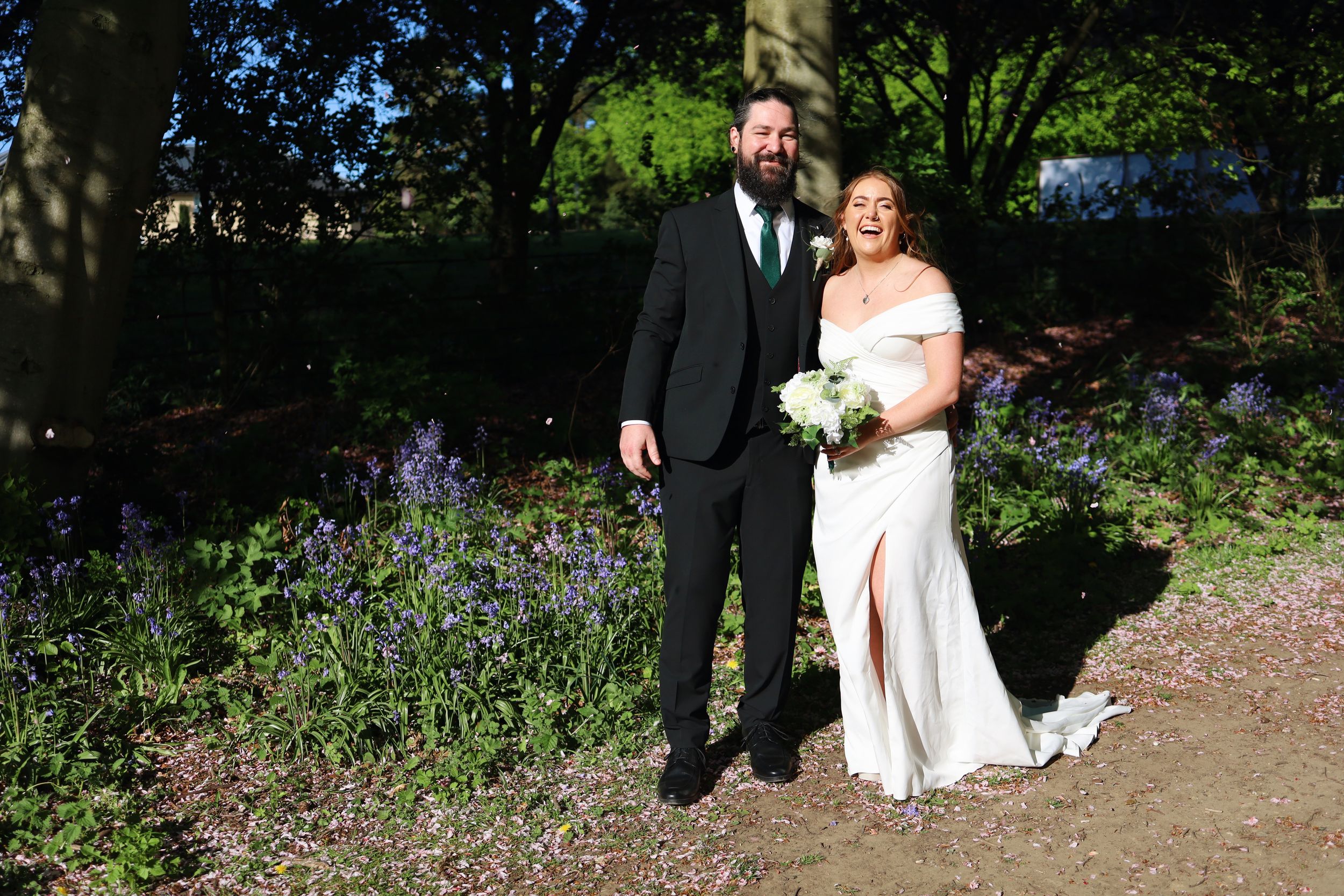 A couple poses in a garden setting surrounded by blooming purple flowers on their wedding day.
