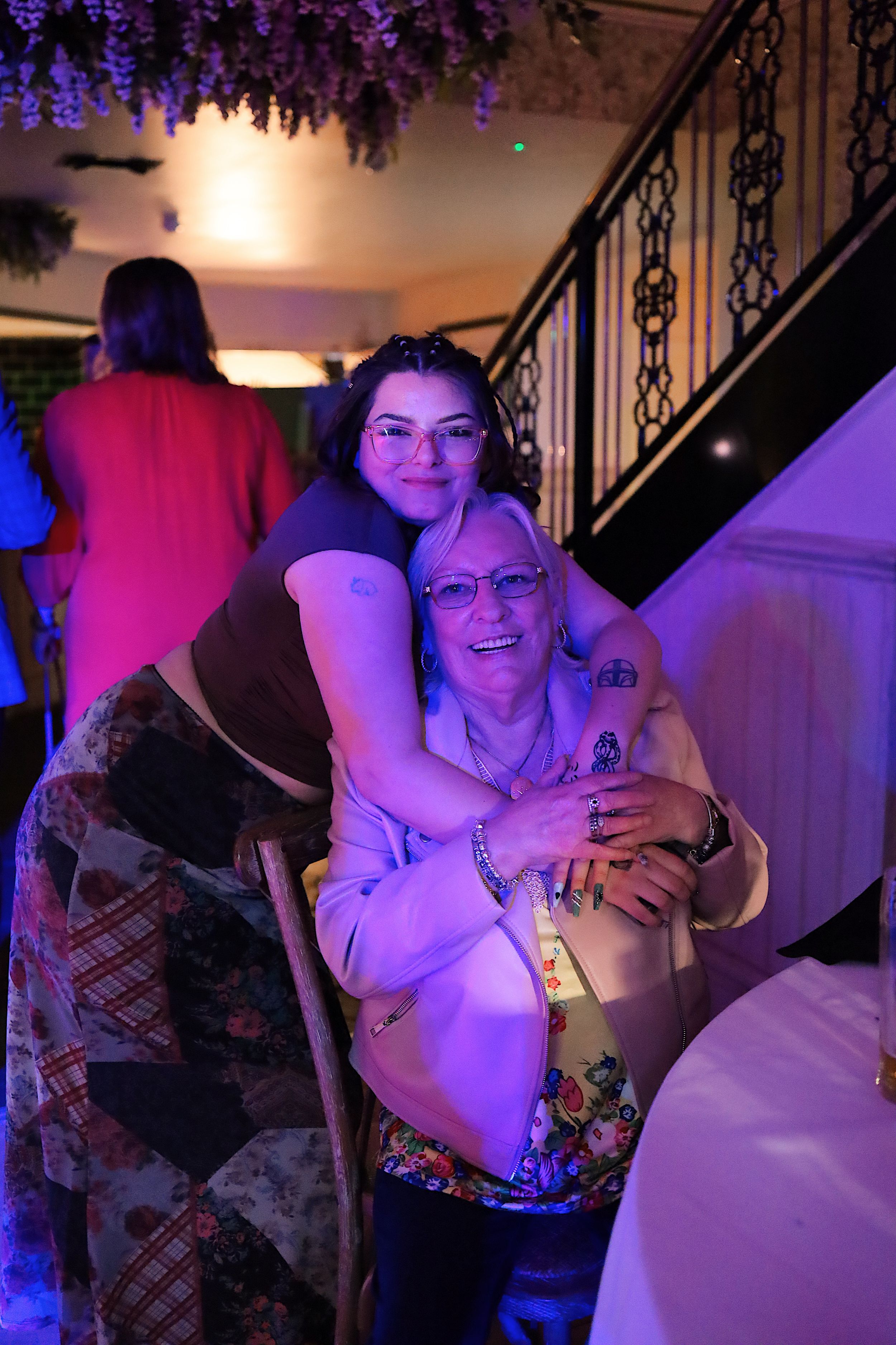 Wedding guests celebrate and dance under purple mood lighting near an ornate staircase.