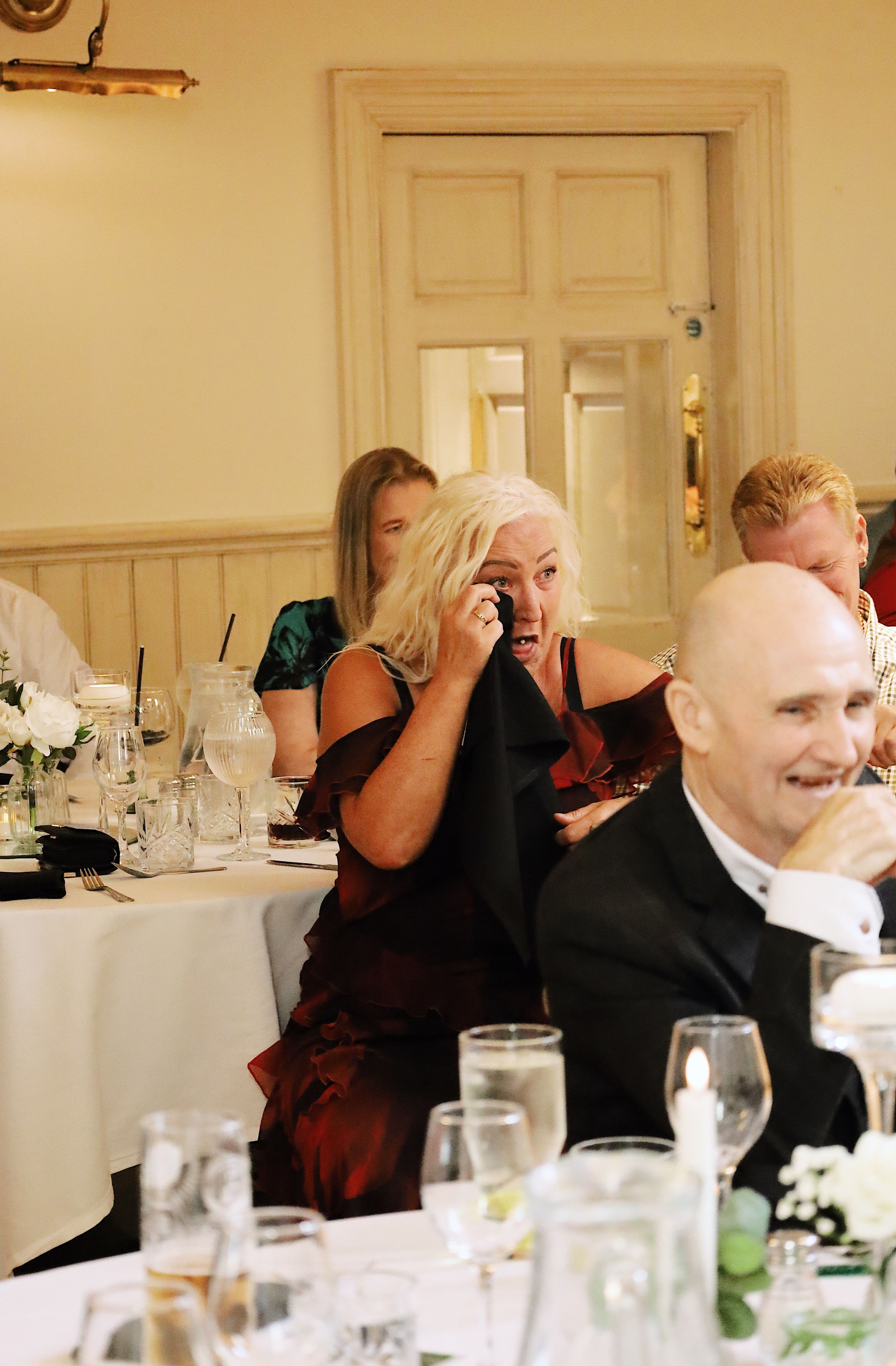 Wedding reception guests seated at tables with white linens in an elegant dining room.
