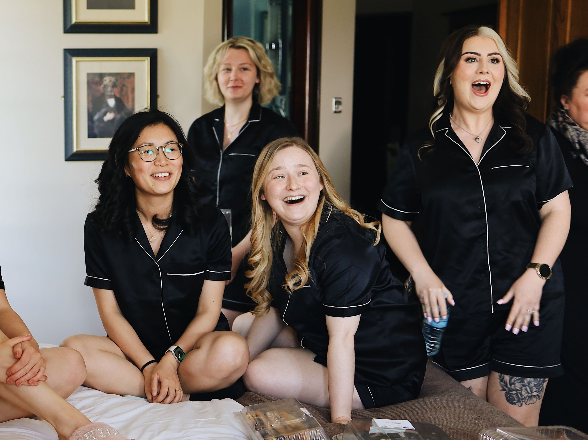 A group in black silk robes shares laughter during pre-wedding preparations.