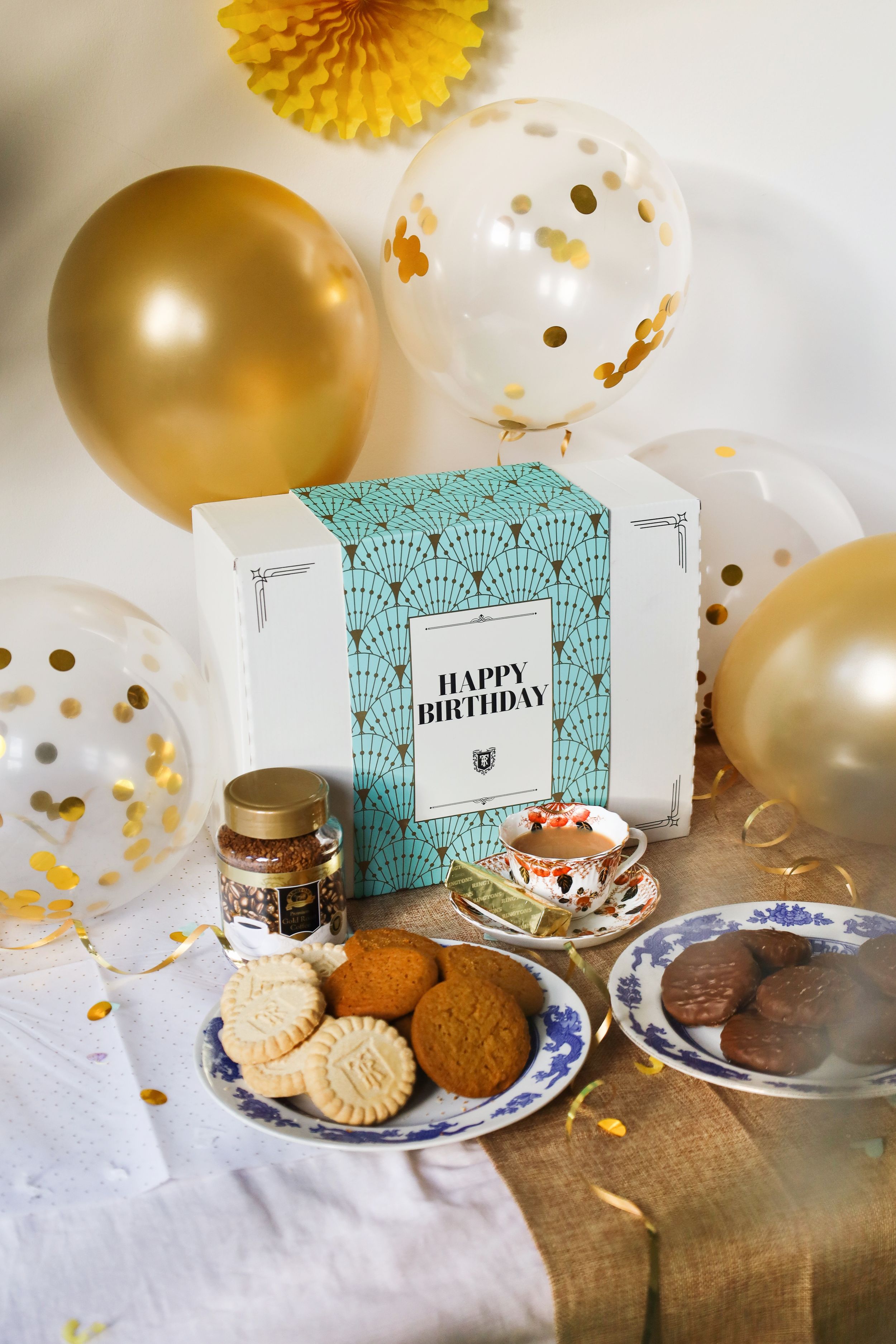 Birthday celebration setup with gold balloons, cookies and teal decorative cards.