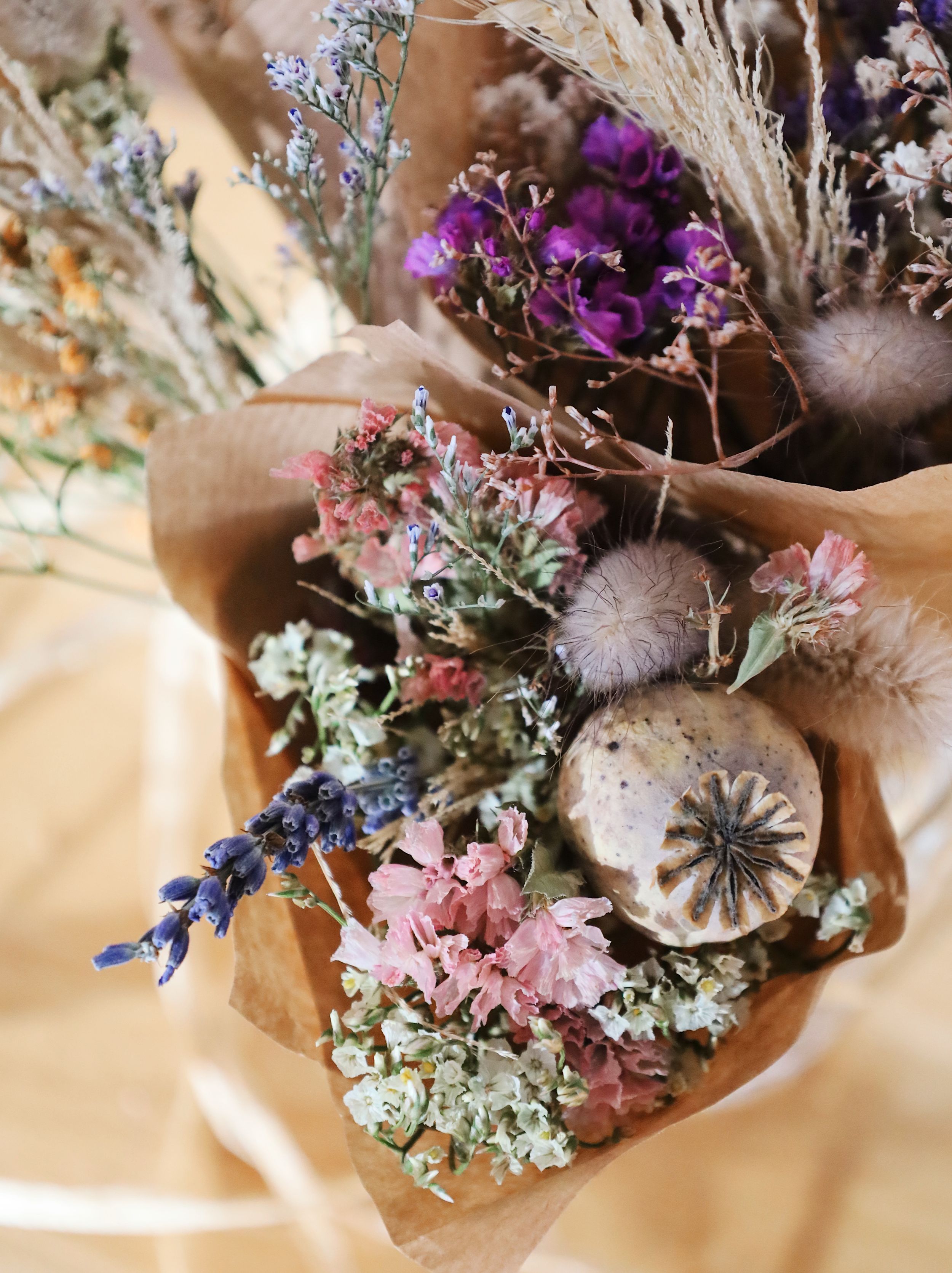 Dried flower arrangement with purple blooms and natural elements on beige background.