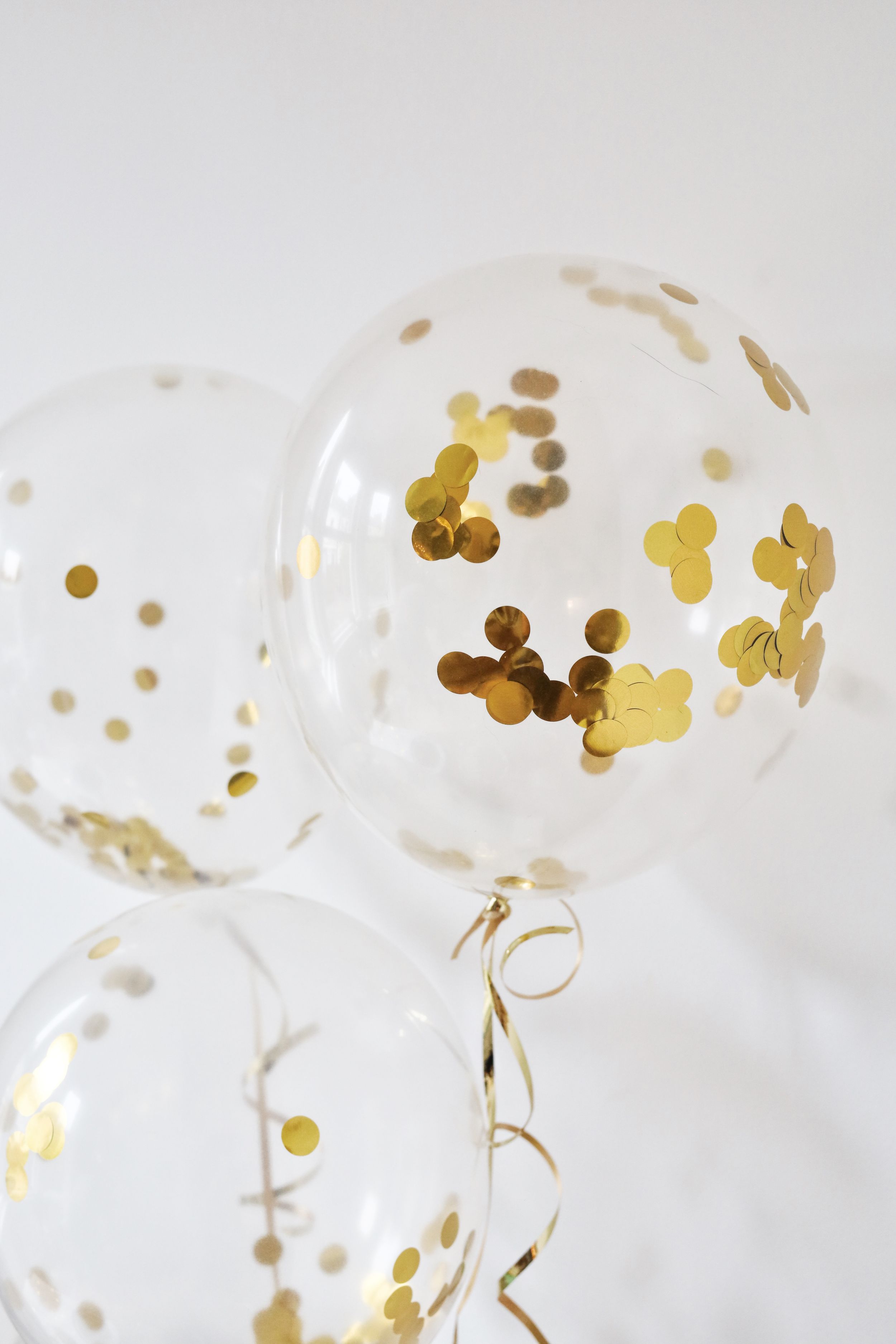 Clear balloons filled with gold confetti against white background.