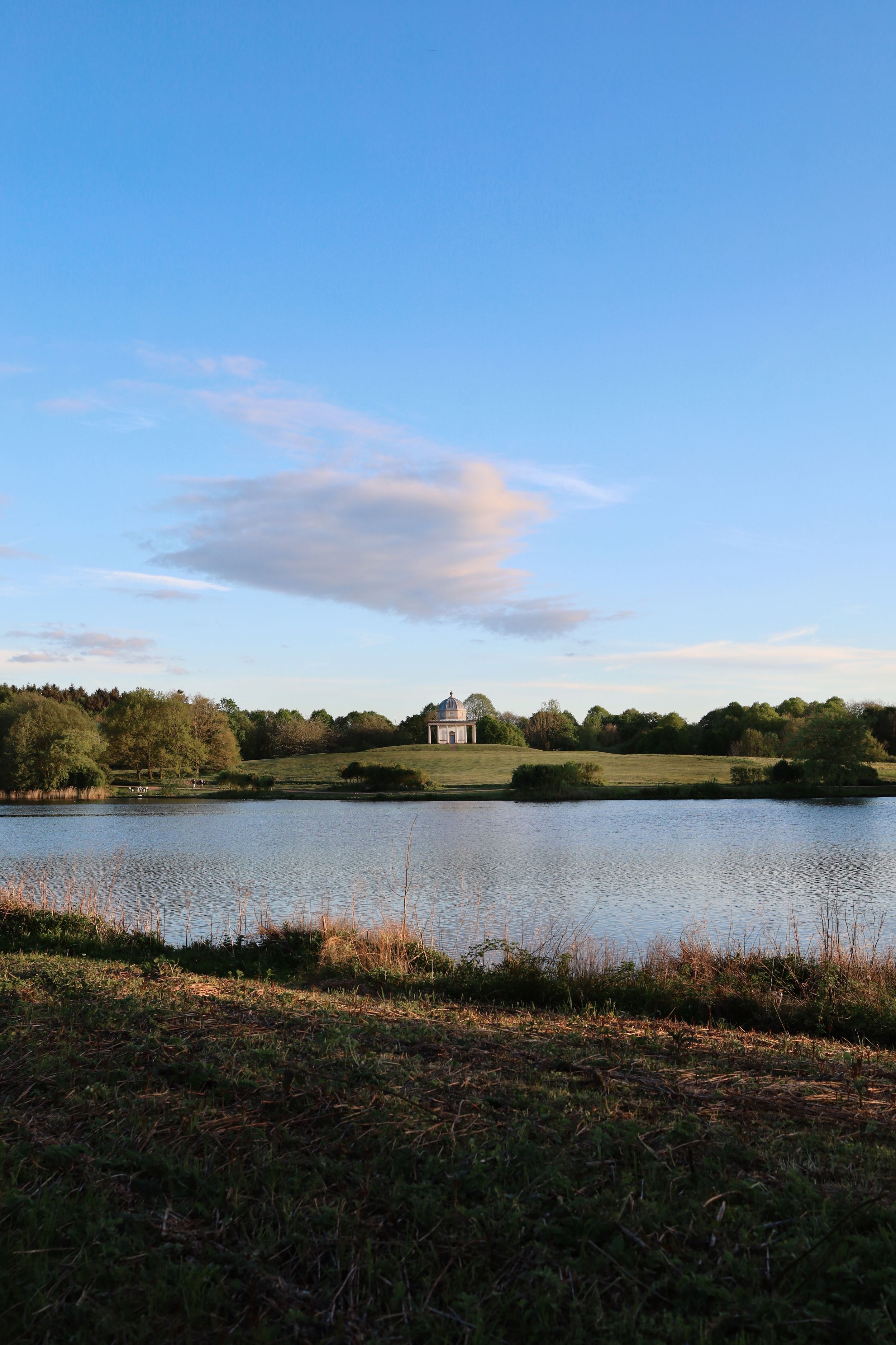 Panoramic landscape view of a lake with classical pavilion structure in the distance.