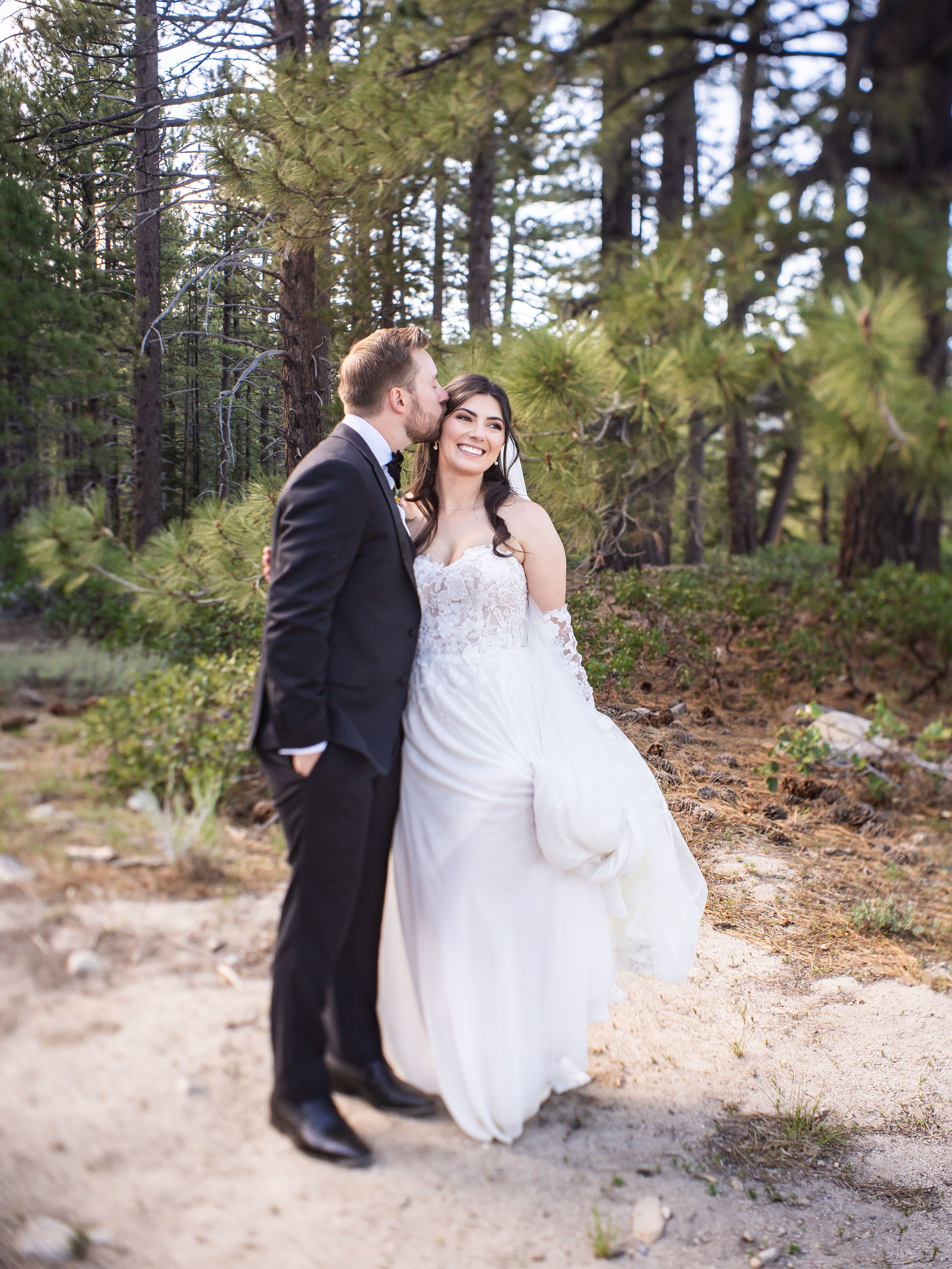 A couple shares a romantic moment together against a backdrop of pine trees in an outdoor forest setting.