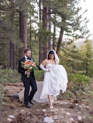 A couple shares playful moments on a forest path surrounded by tall pine trees and natural scenery.