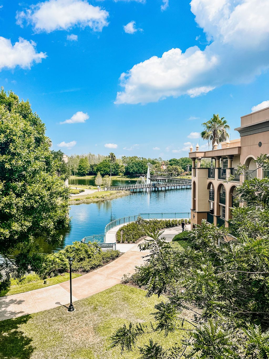 Waterfront view of resort buildings with palm trees, walkways and boat dock under blue skies.