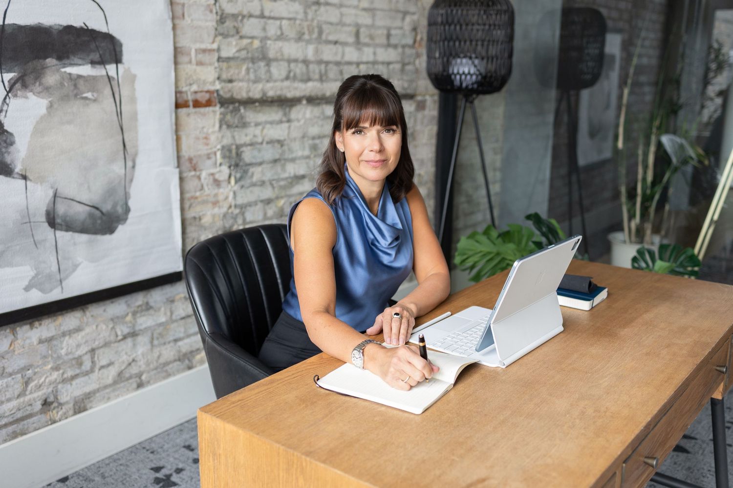 Confident female professor in a blue blouse sitting at a desk during a personal branding photoshoot in London, Ontario.