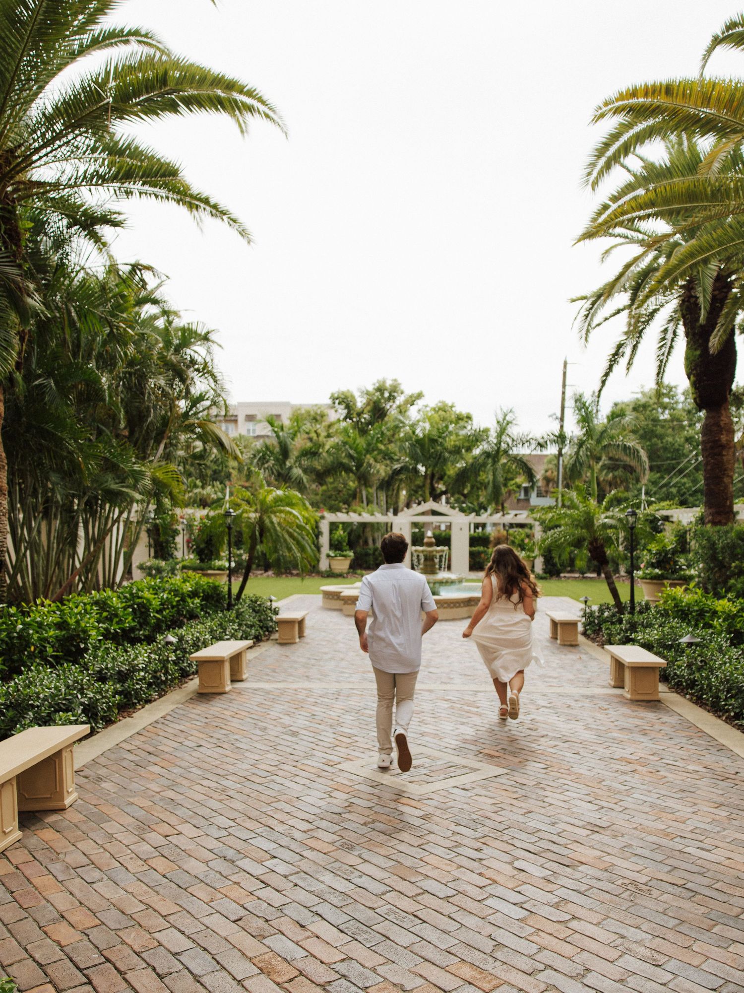 Couple walking away on a palm-lined brick pathway at a tropical resort.