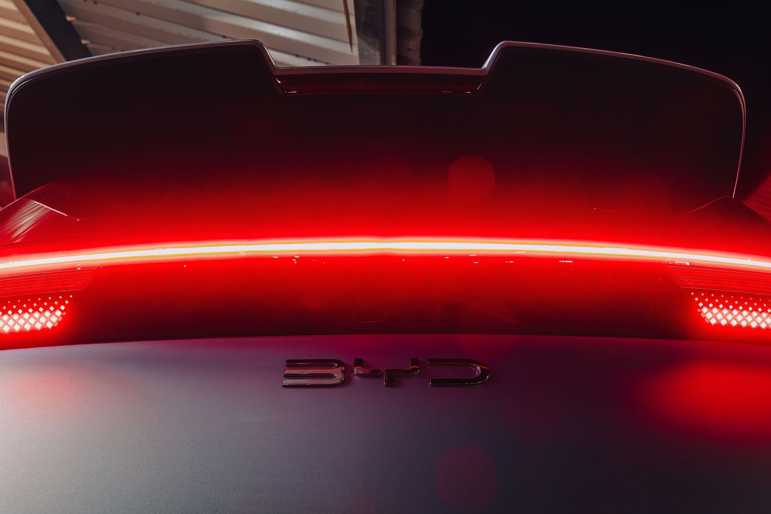 Close-up view of a BYD Dolphin Surf  rear LED light bar and badge in dramatic lighting.