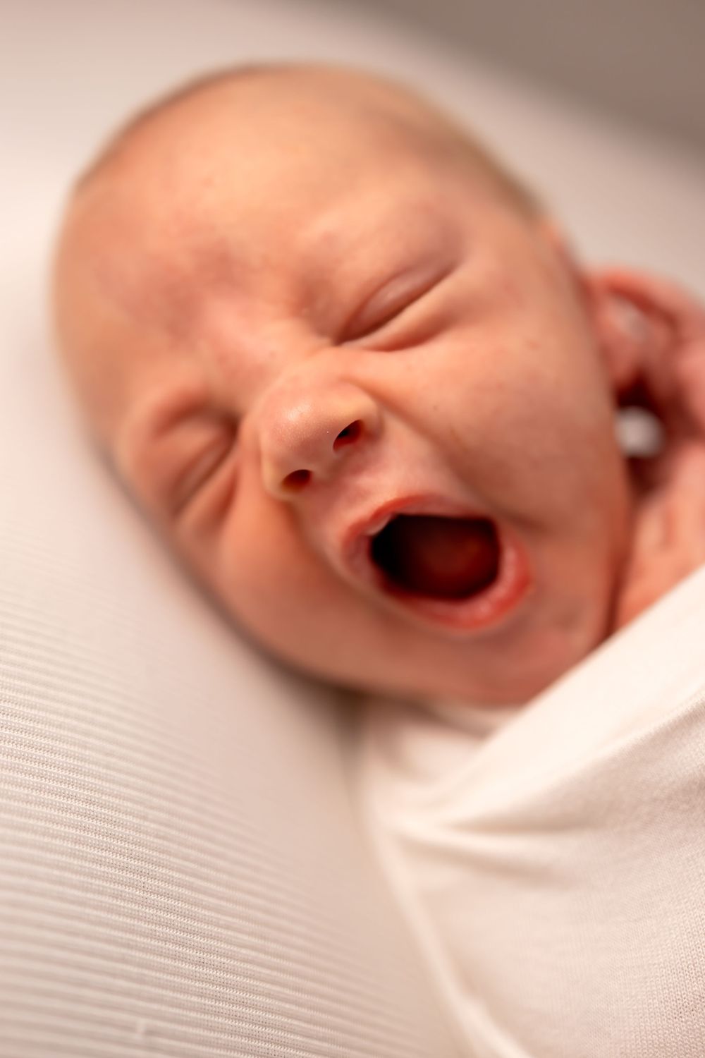 Eleven sequential close-up photos show a newborn yawning while lying on soft white fabric.