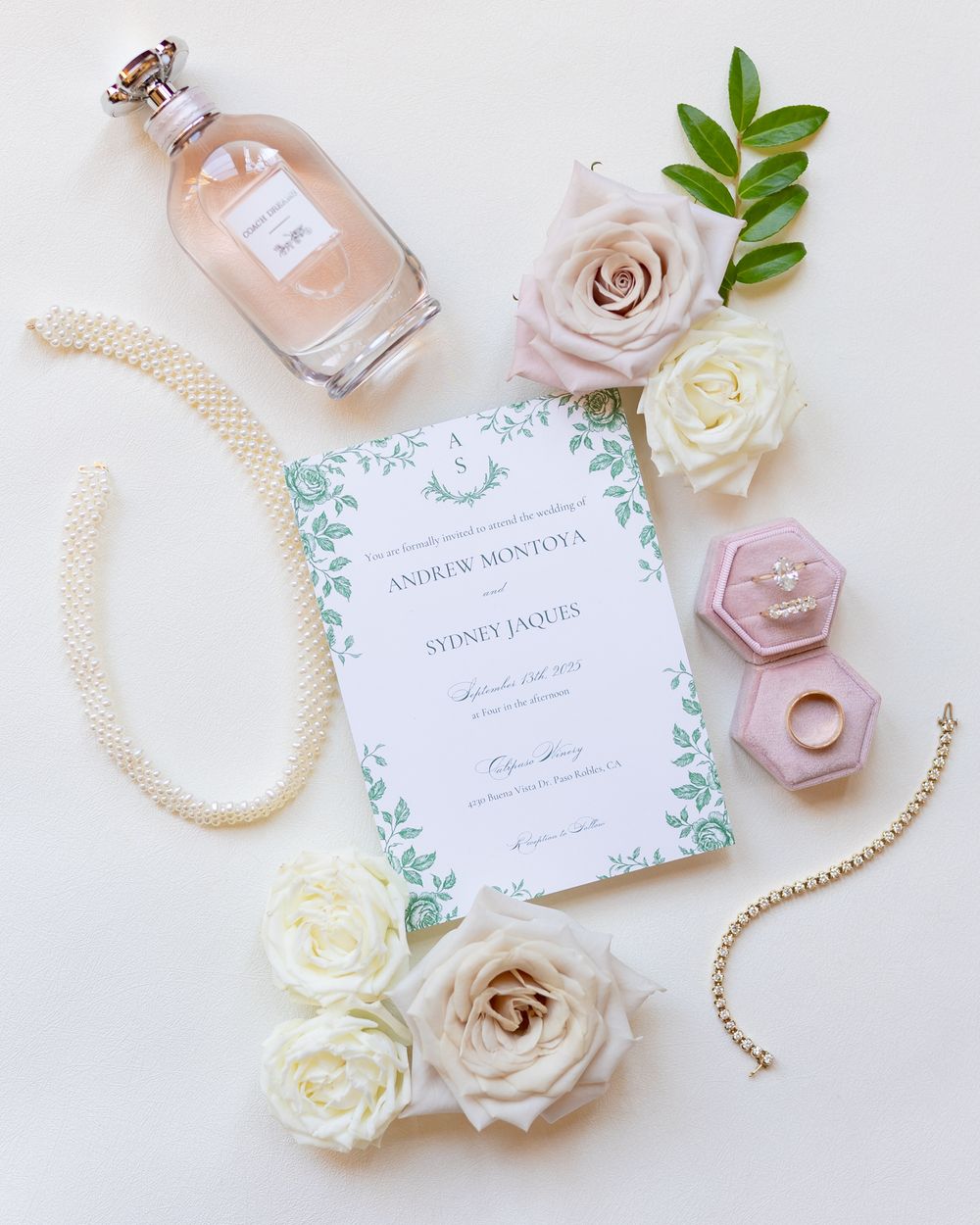 Elegant wedding invitation suite with white and pink roses, pearl necklace, and perfume bottle on light background.