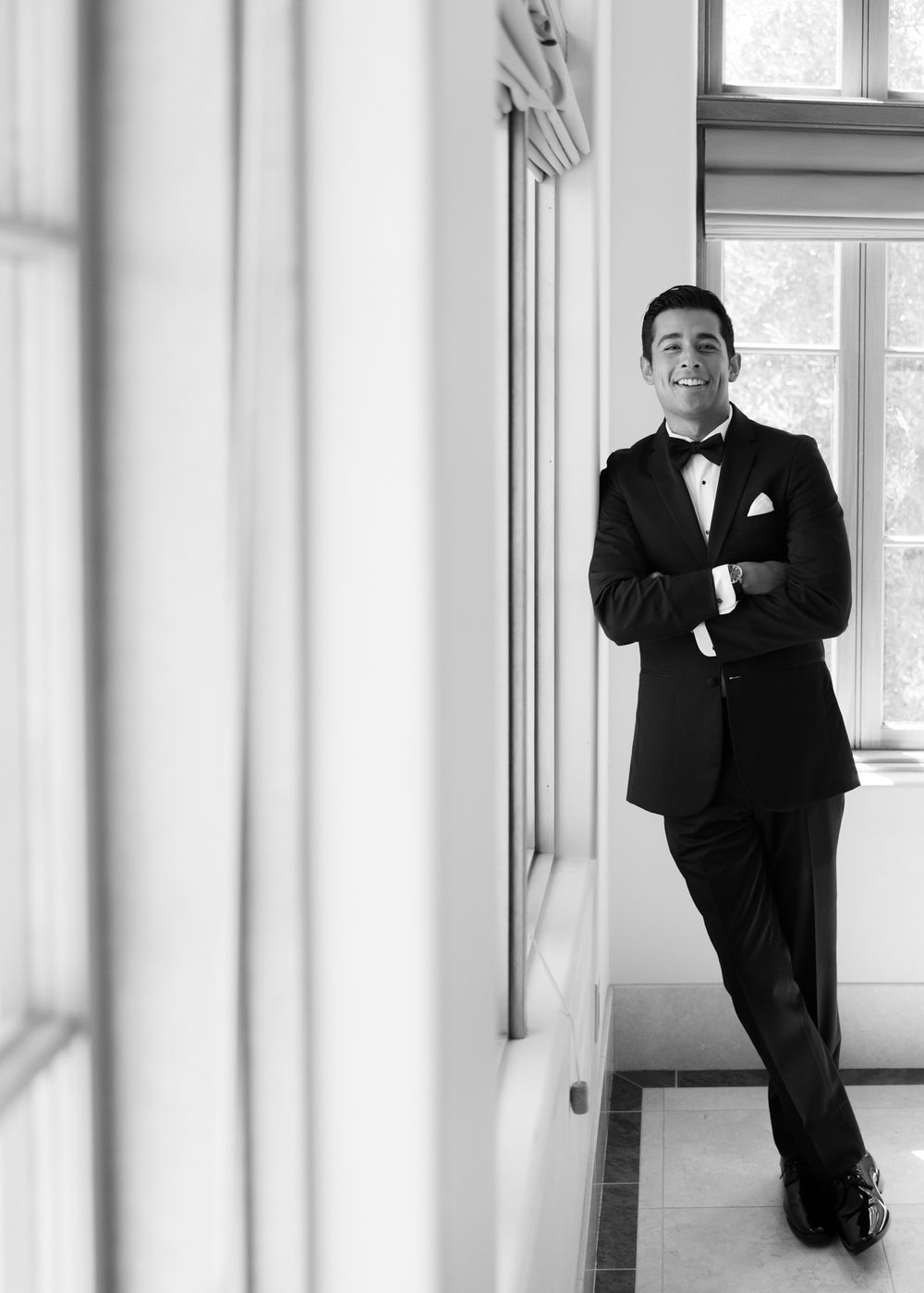 A panoramic series of black and white portraits showing a person in a tuxedo posing against a white wall with windows.