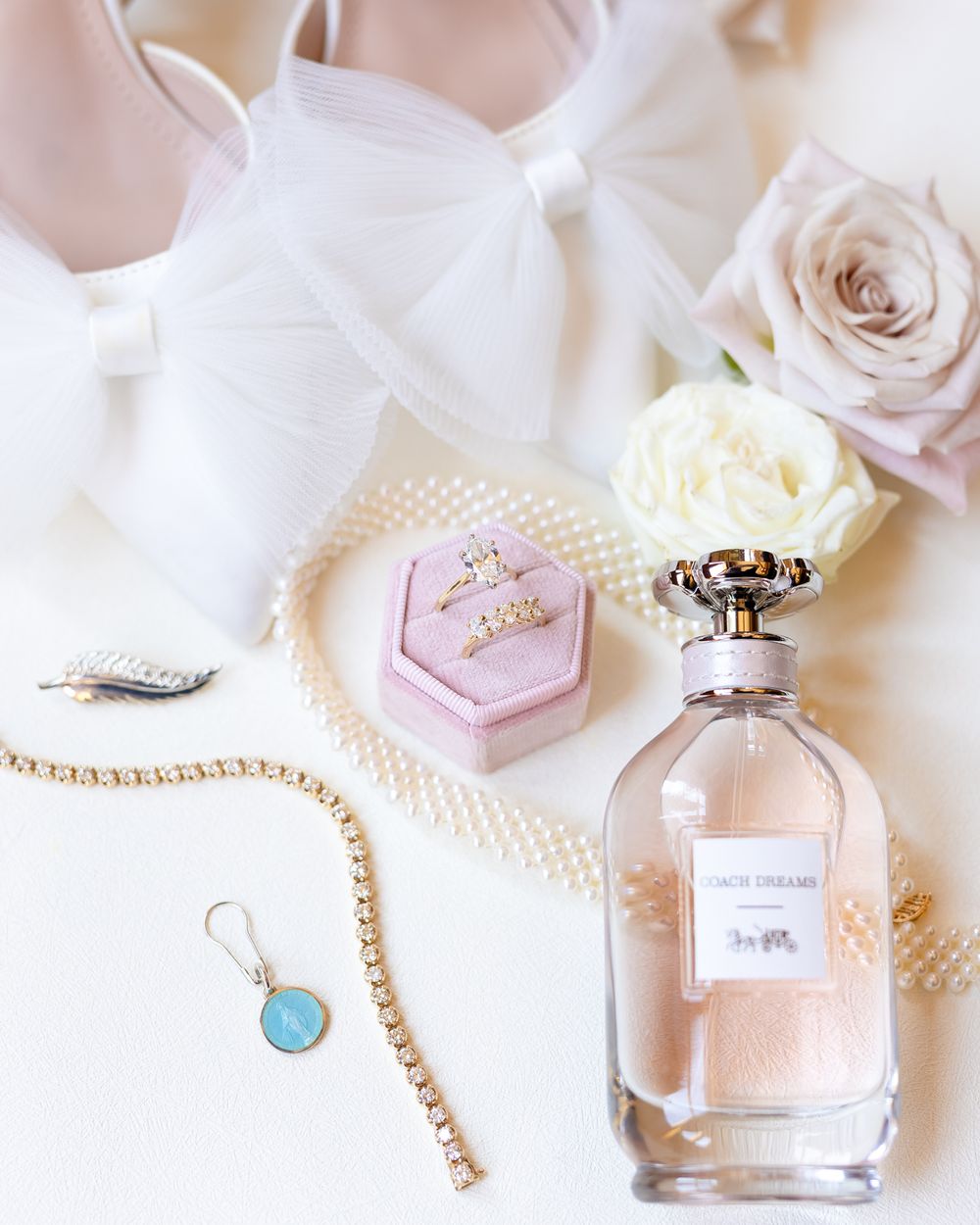 Elegant perfume bottles and jewelry arranged with soft pink roses and white decor on a light background.