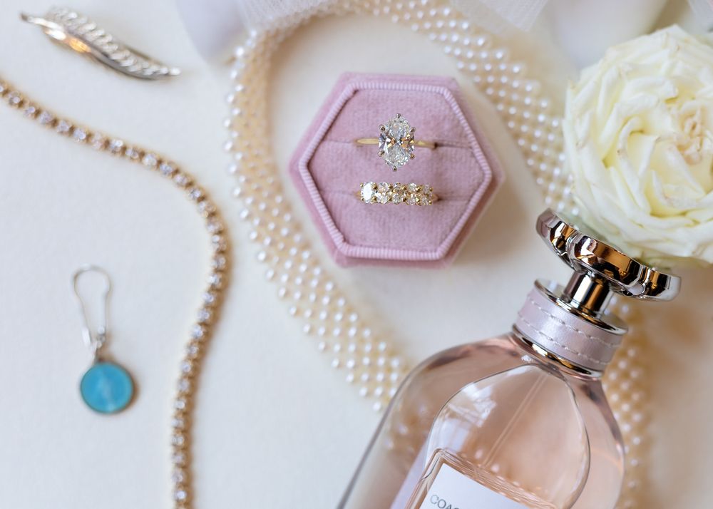 Elegant flatlay with perfume bottle, pink hexagonal jewelry dish, pearls, and white roses on light background.