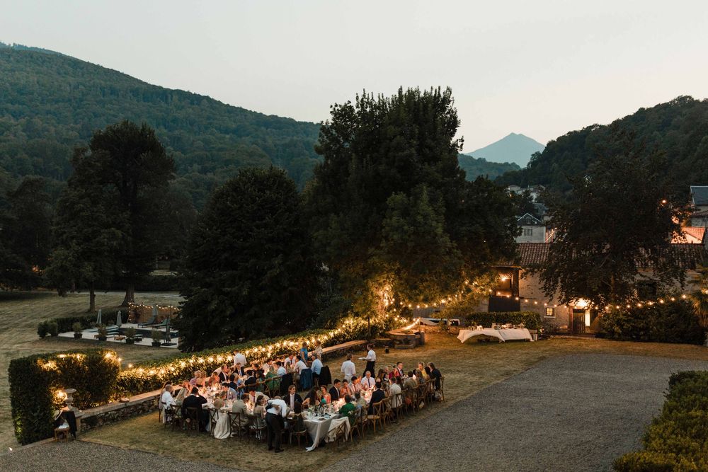 A long outdoor dining table illuminated by string lights at dusk in a mountainous setting.
