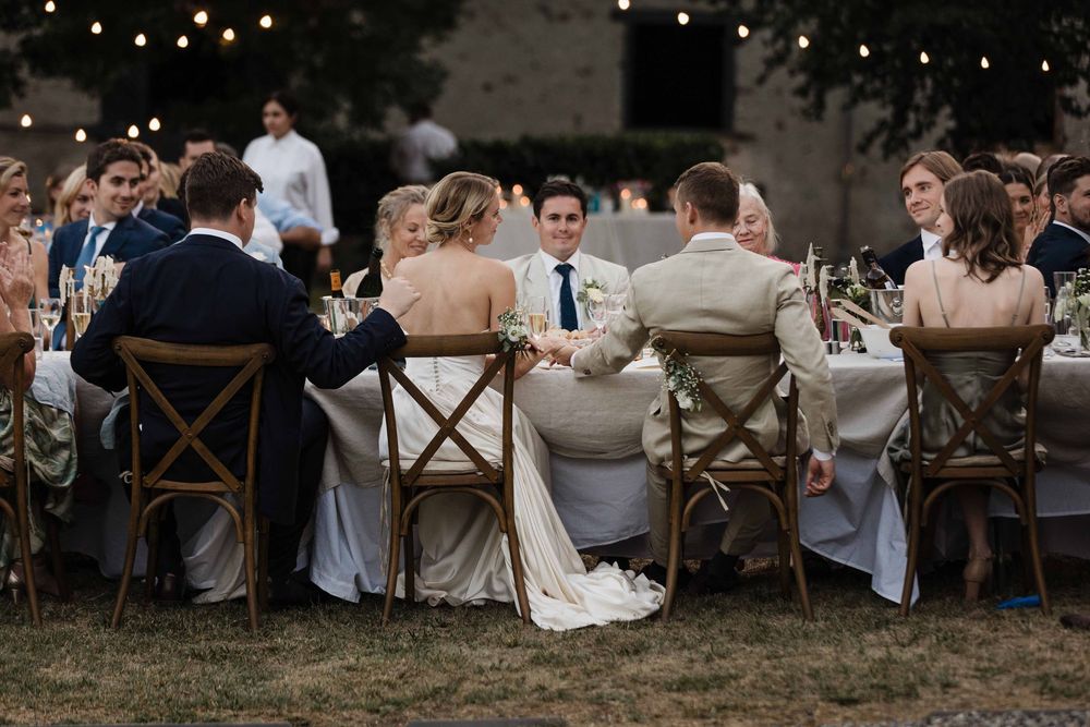 Guests seated at an elegant outdoor wedding reception dinner under string lights at dusk.