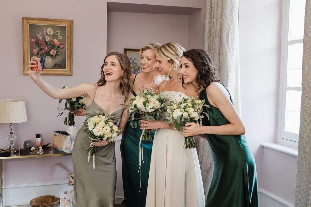 Wedding bridesmaids in emerald green dresses share champagne toasts during celebration preparations.