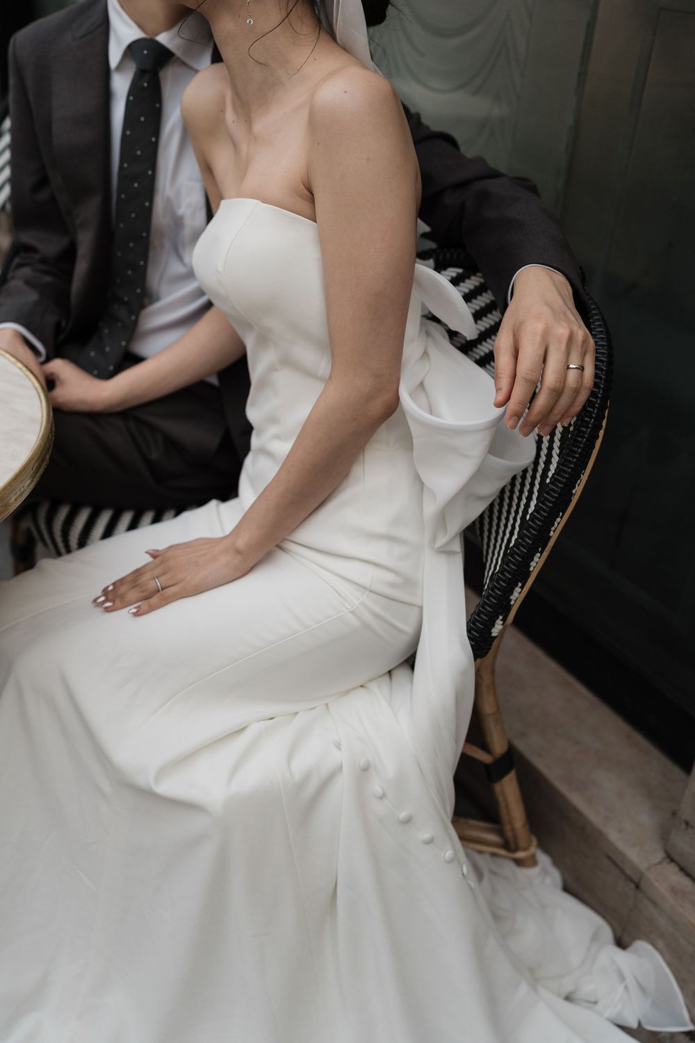 Close-up view of a bride in an elegant white strapless wedding gown sitting on a bistro chair.