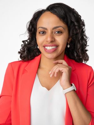 Professional woman in red blazer and white top smiling confidently with hand on chin against white background.