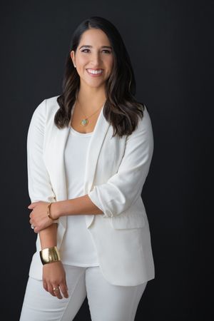 Professional portrait of woman in white suit against dark background.
