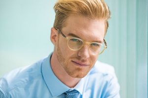 Professional wearing light blue shirt and glasses works in modern office environment with natural lighting.