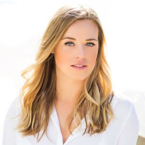 Professional headshot of a woman with blonde wavy hair wearing a white blouse against a light background.