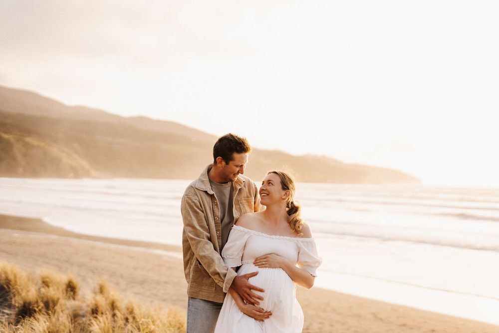 Romantic couple shares a tender moment at sunset on a scenic beach with golden hills in the background.