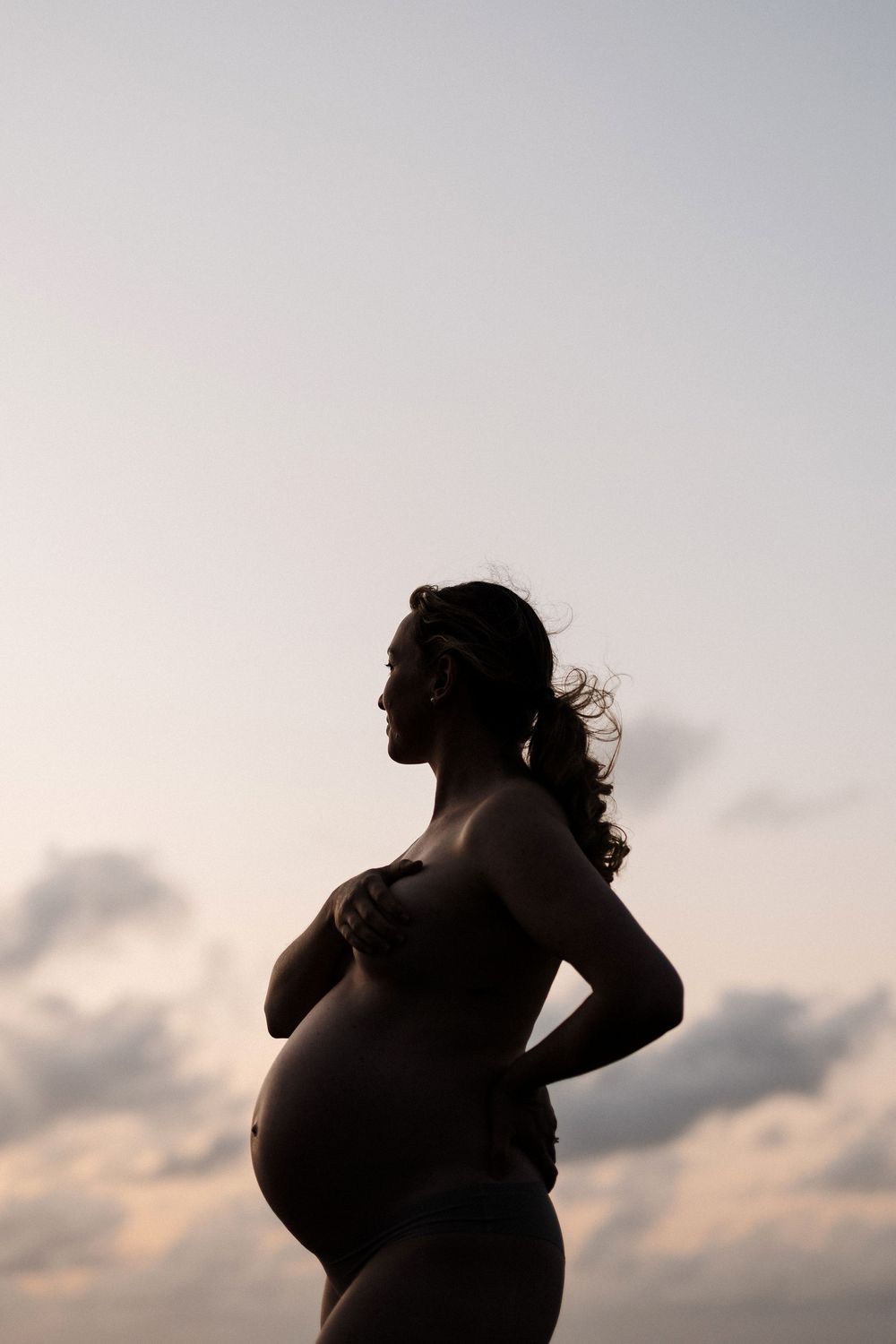 A silhouette of a pregnant woman's profile against a sunset sky, showcasing her baby bump in an artistic maternity pose.