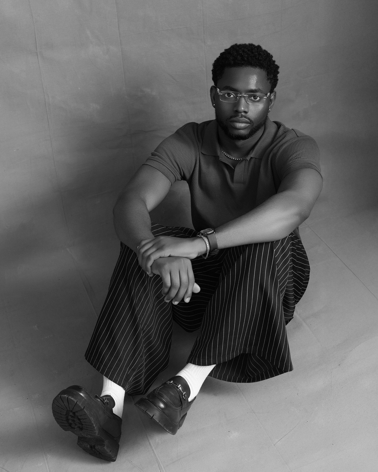 Professional studio portrait of Timi Olumide wearing glasses and a navy quarter-zip sweater against a blue backdrop.