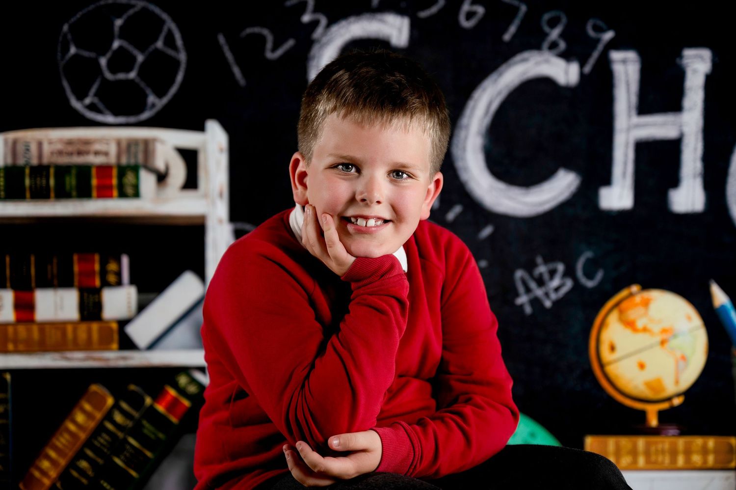 A student in a bright red sweater sits in front of a classroom-style chalkboard with educational elements in the background.