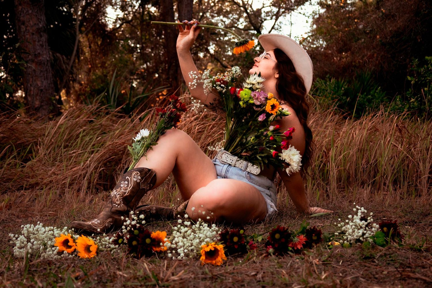Artistic outdoor portrait with flowers and decorative elements in natural setting at sunset.