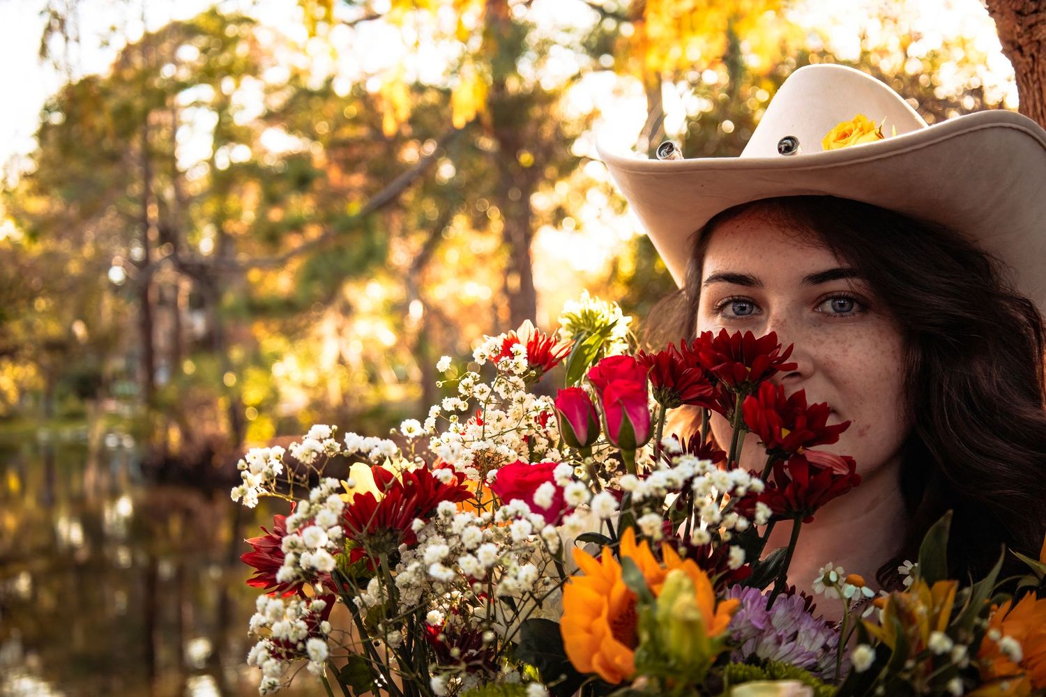Artistic portrait with colorful flower bouquet against autumn forest backdrop.