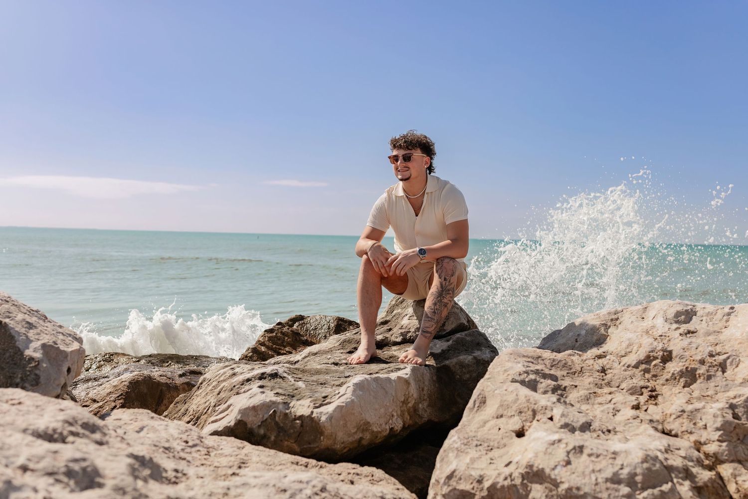 Person lounging on coastal rocks near turquoise ocean water on sunny day.