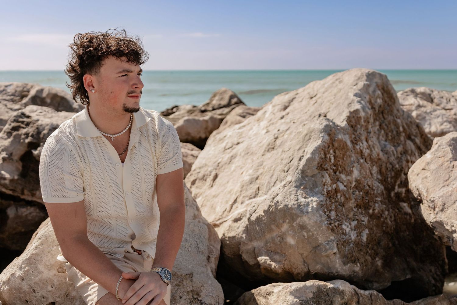 Person resting on large beach rocks with clear blue ocean water in background.