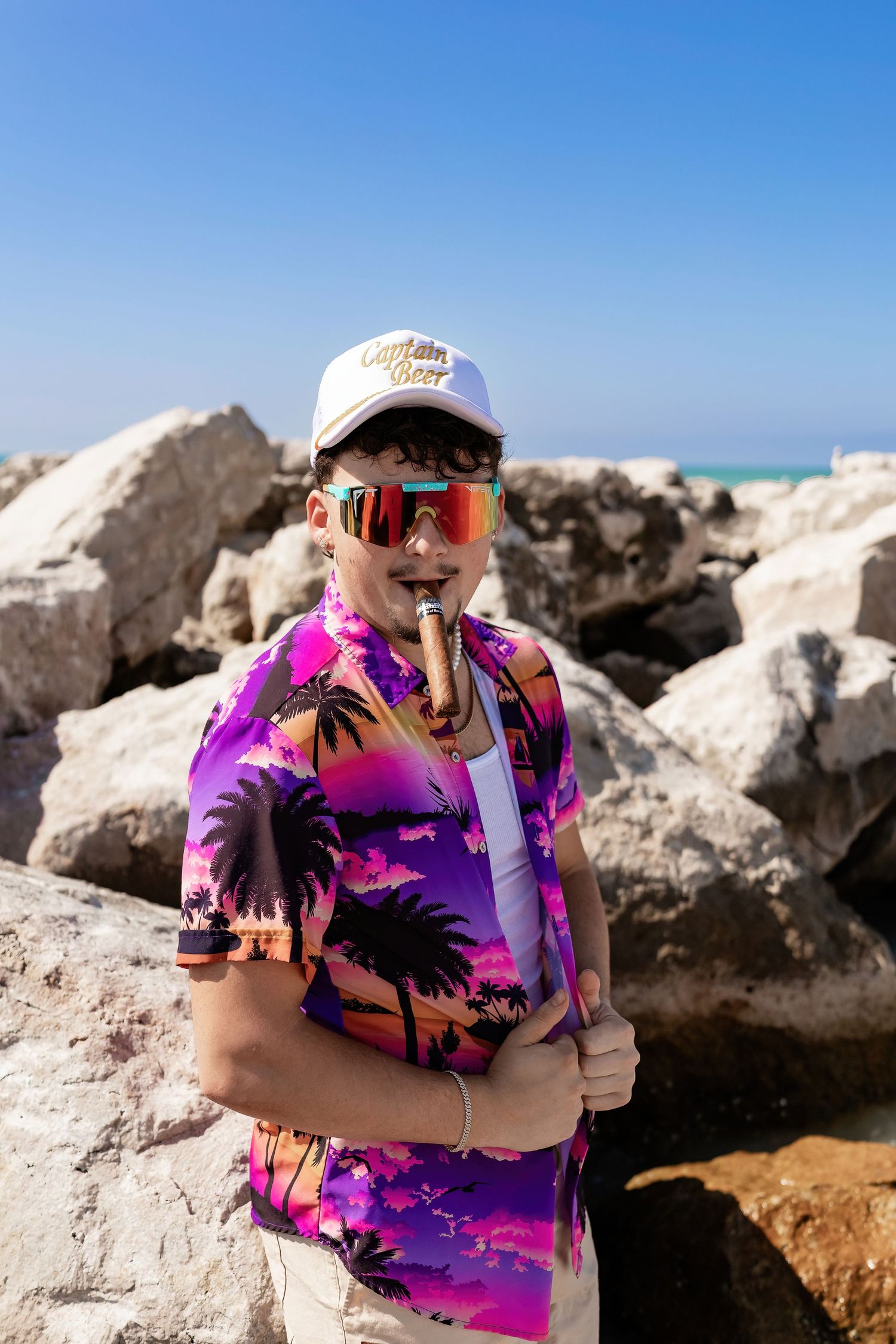 Person in vibrant palm tree print shirt poses on rocky beach overlook.