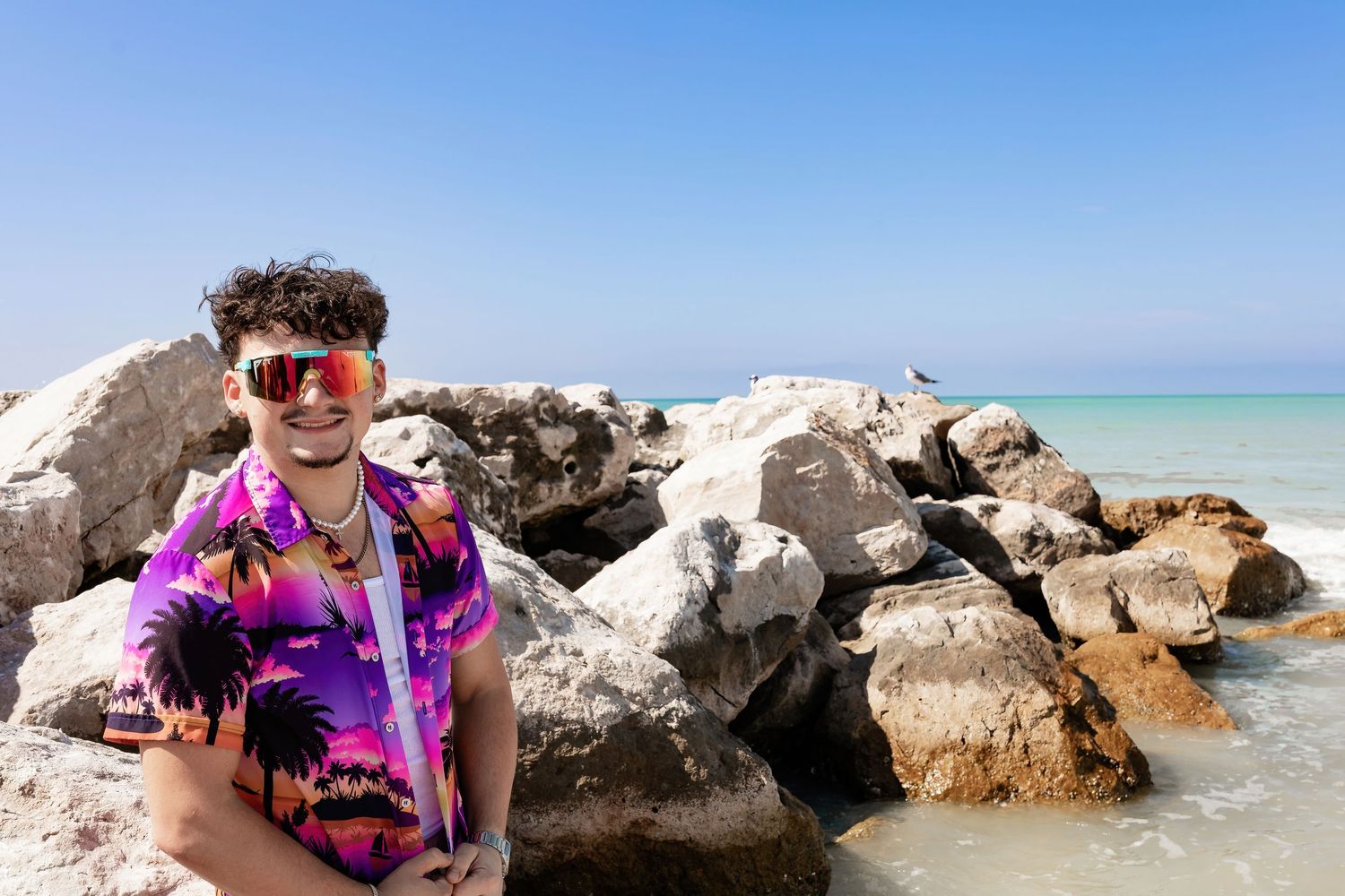 Person in colorful tropical shirt relaxing on coastal rocks by ocean.