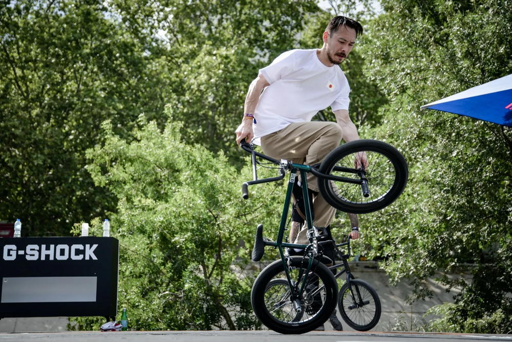Figure de flat BMX en équilibre, exécutée sur deux roues dans un parc ensoleillé.